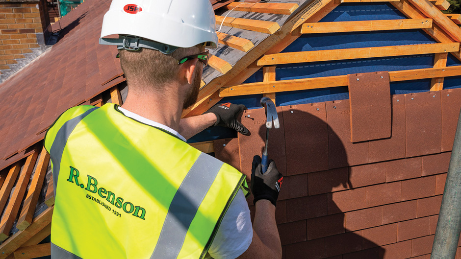 Man hanging new tiles on roof in hi vis, hat and googles