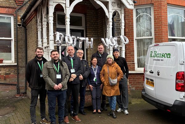 1000th Void Completion for NHG - Picture of 8 people outside appartmants with balloons spelling out 1000th White van with words R. Benson in Green