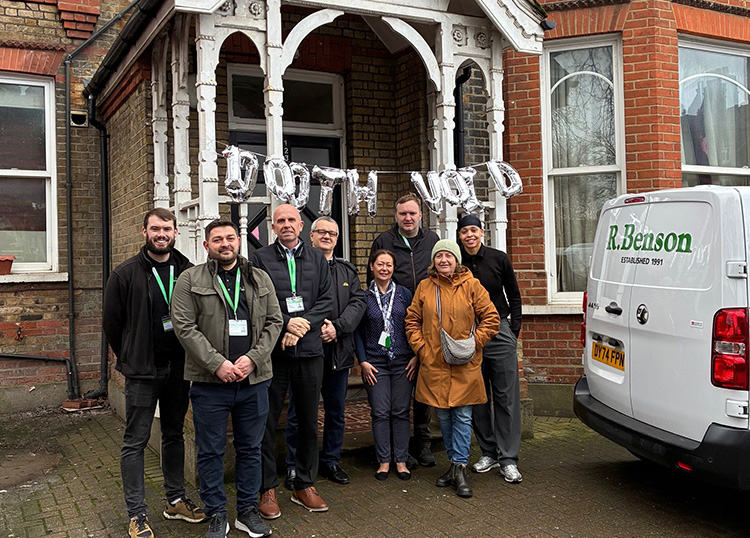 1000th Void Completion for NHG - Picture of 8 people outside appartmants with balloons spelling out 1000th White van with words R. Benson in Green